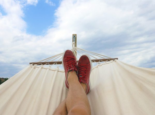 Feet wearing read sneakers on hammock with cloudy blue sky in the distance