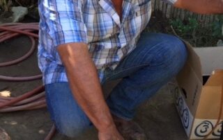 Man in cowboy hat filling or cleaning bottles with a hose