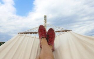 Person relaxing in hammock with red sneakers against blue sky